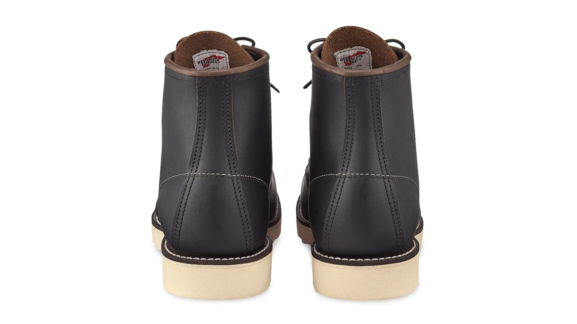 A pair of black leather moc toe boots on cream wedge soles, seen straight on from the heels