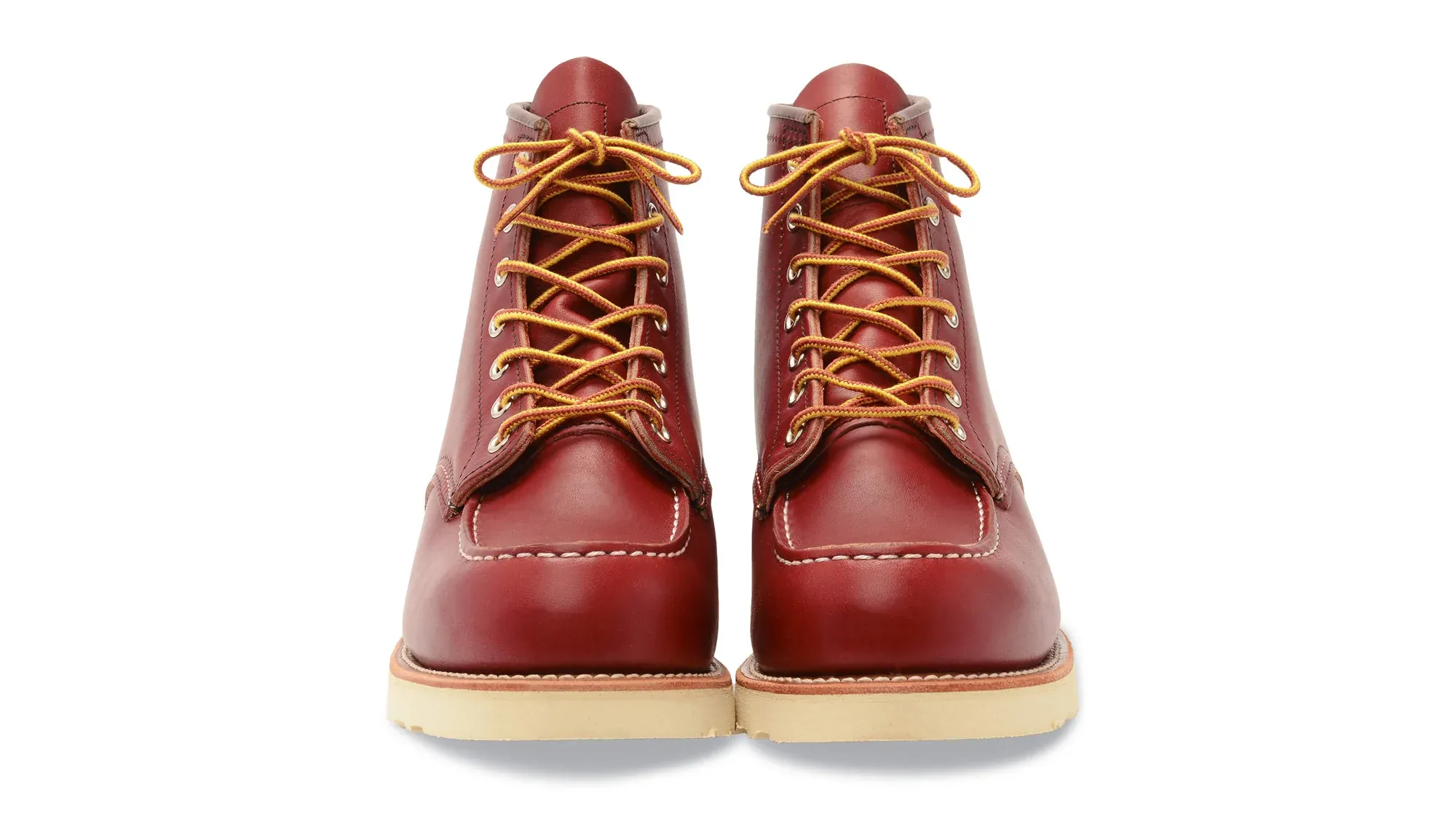A pair of red leather moc toe boots on cream wedge soles, seen straight on from the front