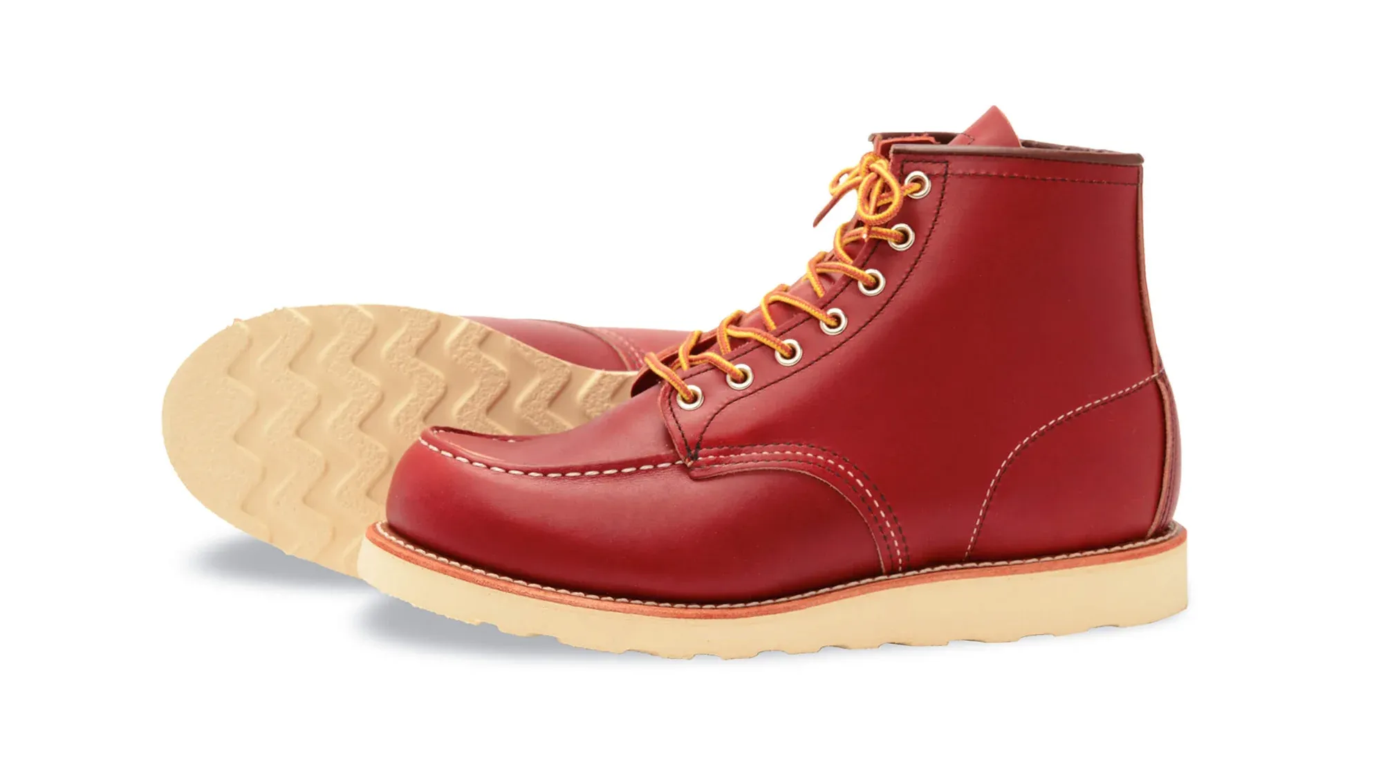 A red leather moc toe boot on a cream wedge sole, tipped on its side to show the sole