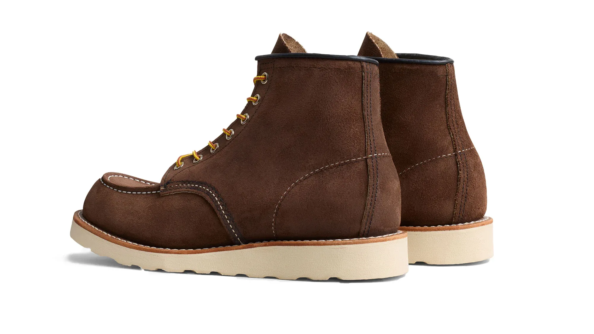 A pair of chocolate roughout suede moc toe boots on cream wedge soles, seen from behind at an angle