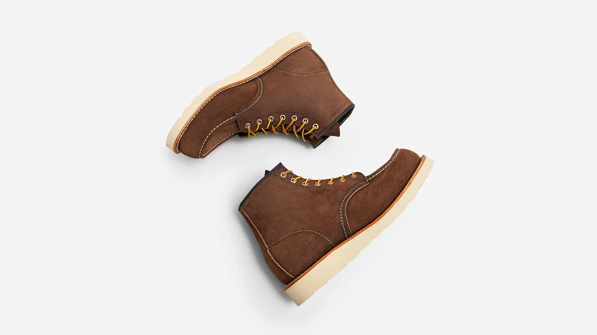A pair of chocolate roughout suede moc toe boots on cream wedge soles, seen from above on a grey ground
