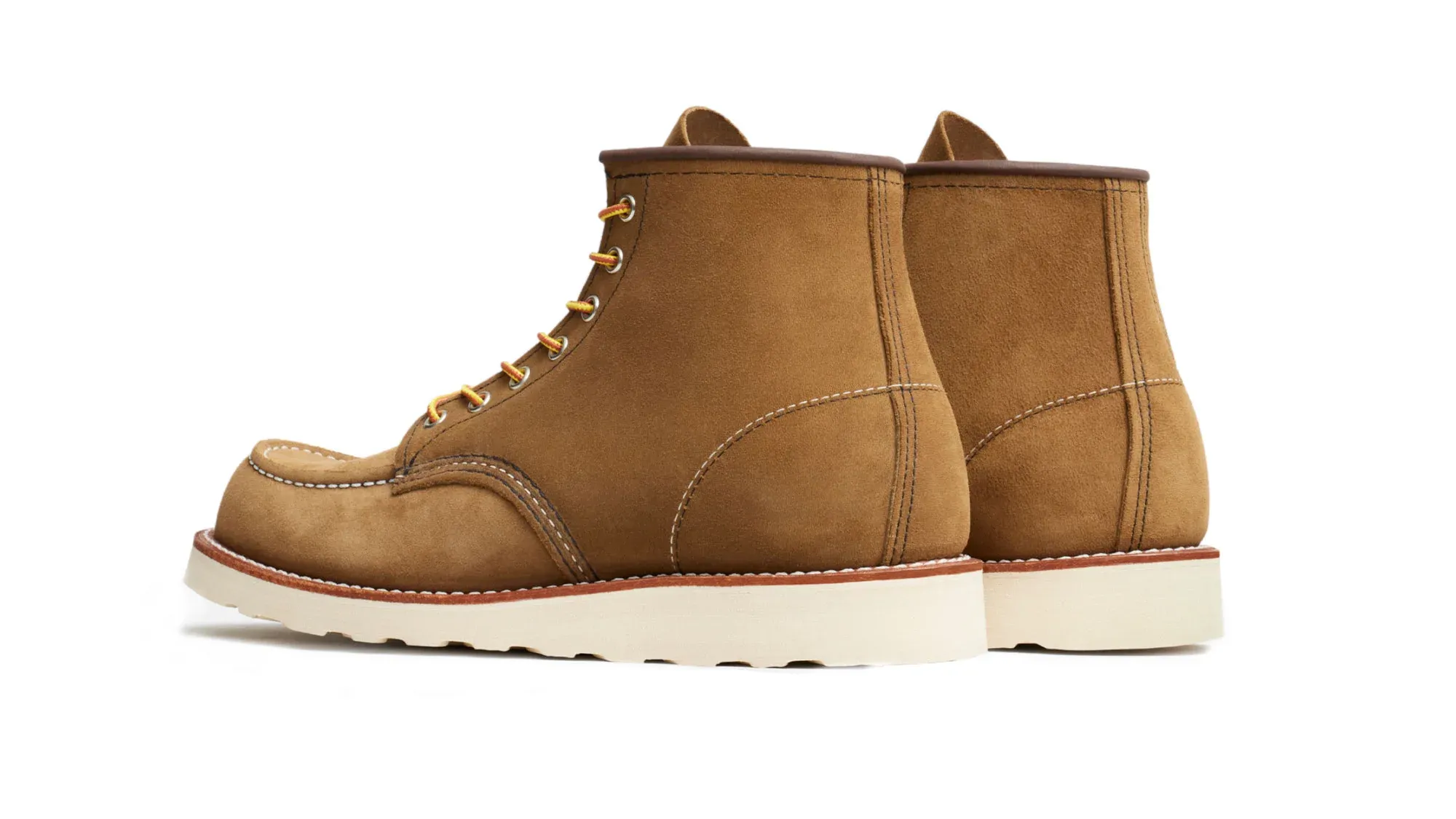 A pair of olive roughout suede moc toe boots on cream wedge soles, seen from behind at an angle