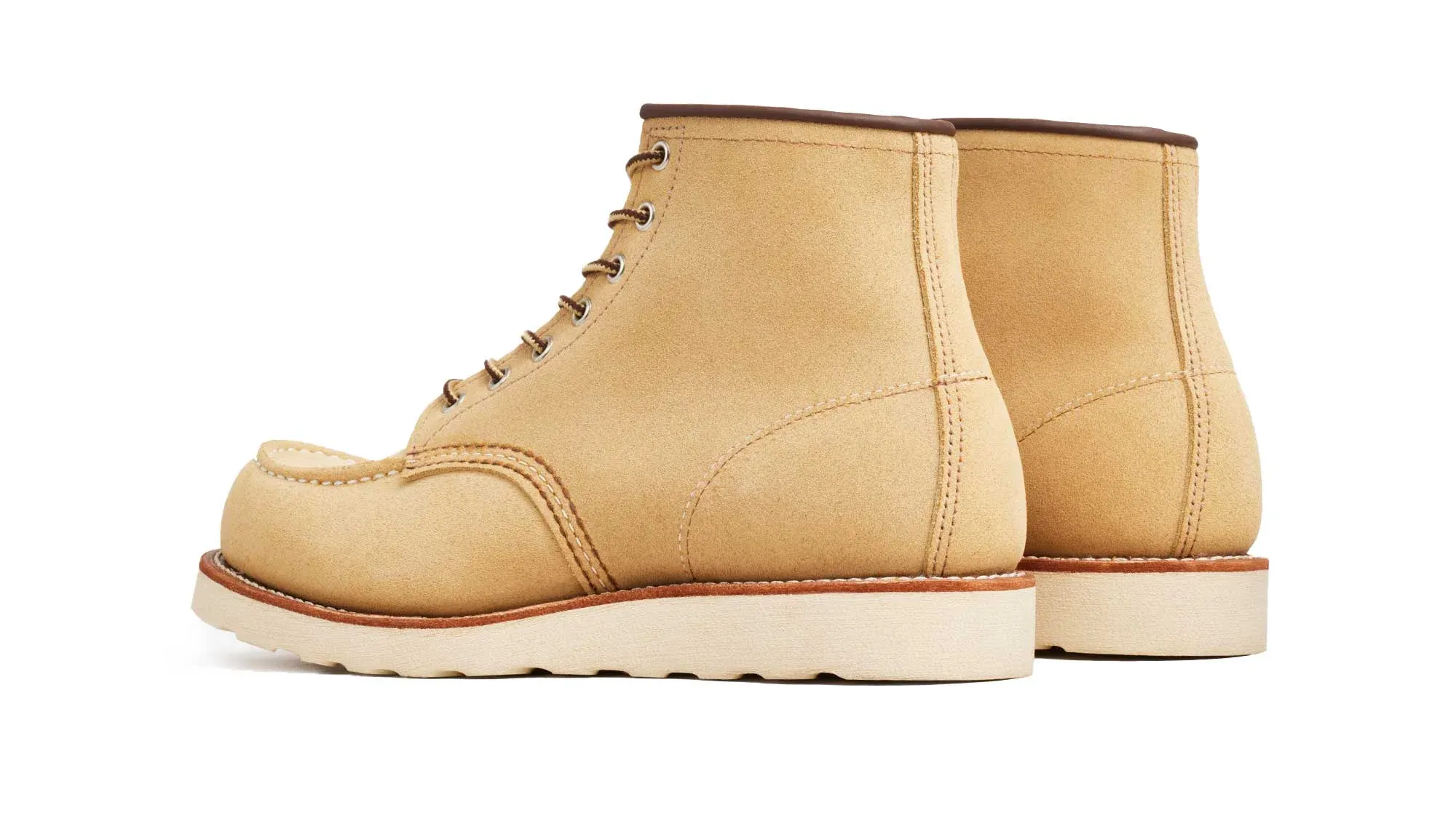 A pair of sand roughout suede moc toe boots on cream wedge soles, seen from behind at an angle