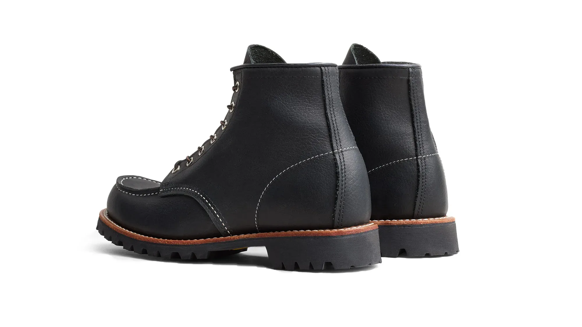 A pair of black leather moc toe boots on black lug soles, seen from behind at an angle