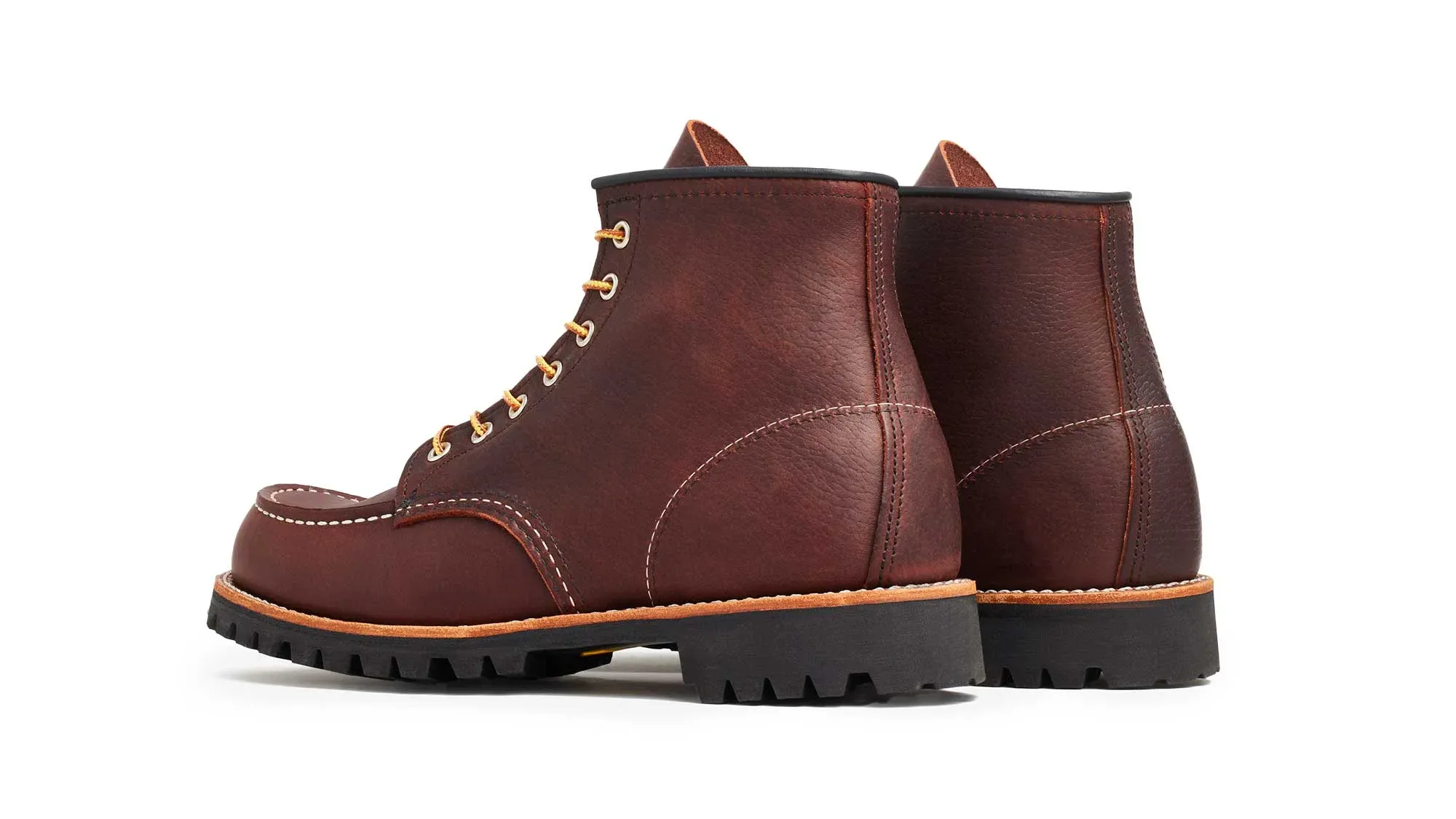 A pair of oxblood leather moc toe boots on black lug soles, seen from behind at an angle