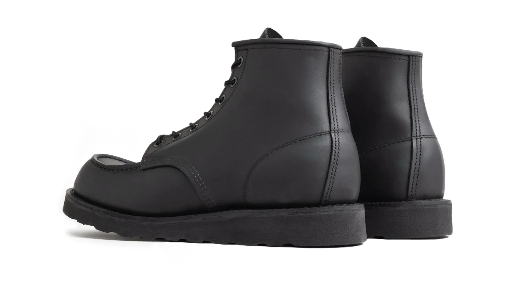 A pair of black waxed suede moc toe boots on black lug soles, seen from behind at an angle