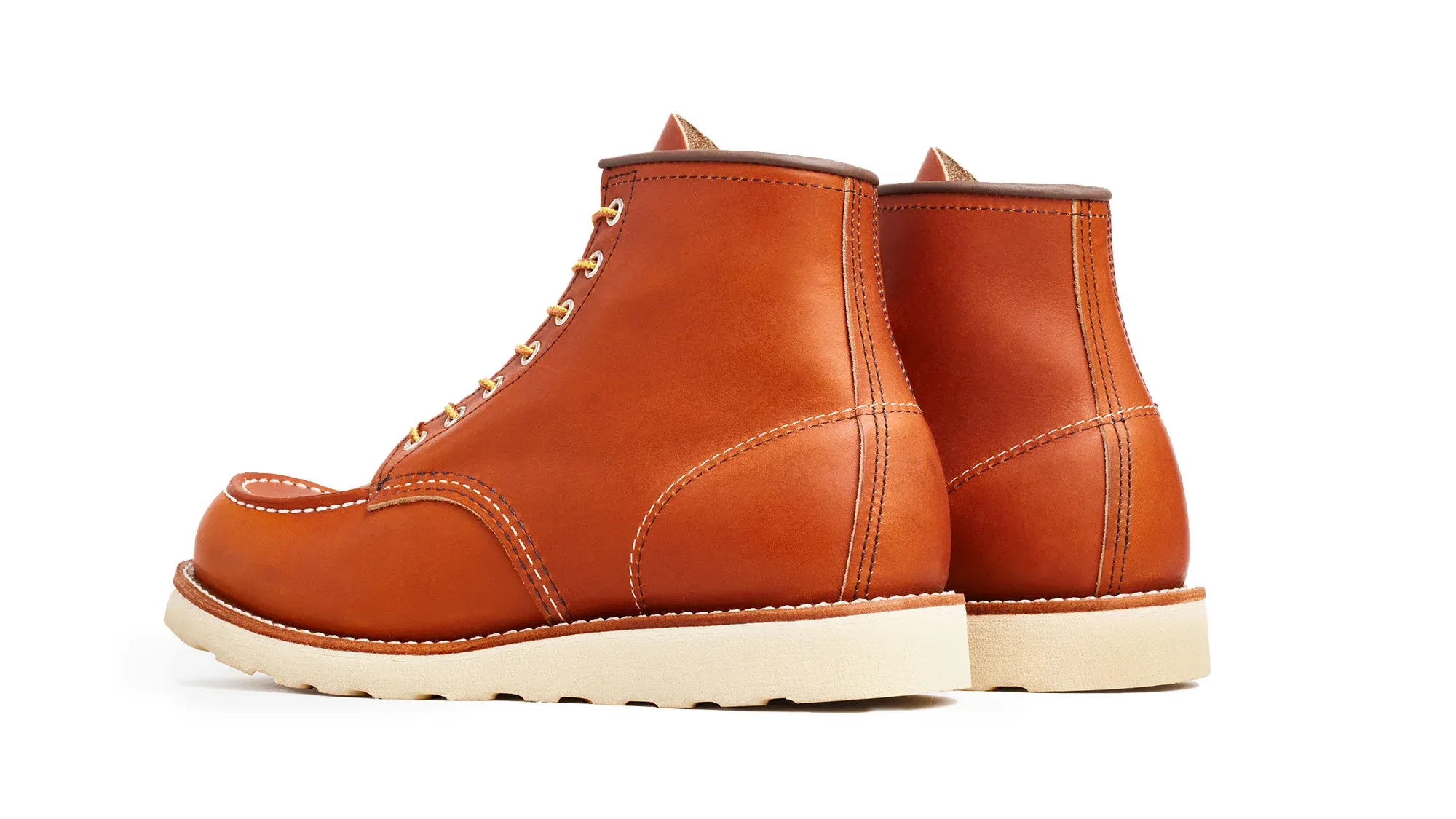 A pair of amber leather moc toe boots on cream wedge soles, seen from behind at an angle