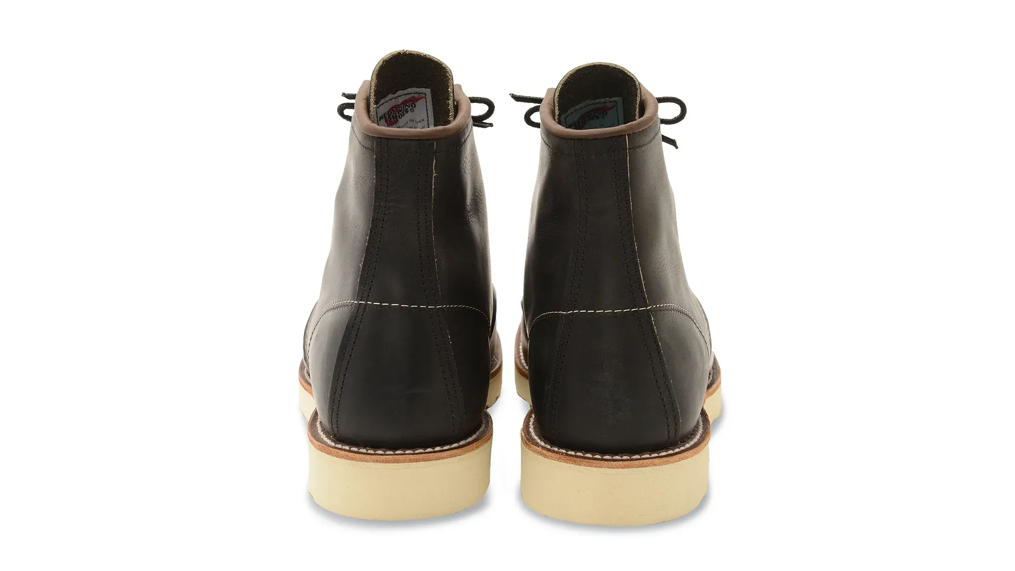 A pair of charcoal leather moc toe boots on cream wedge soles, seen straight on from the heels