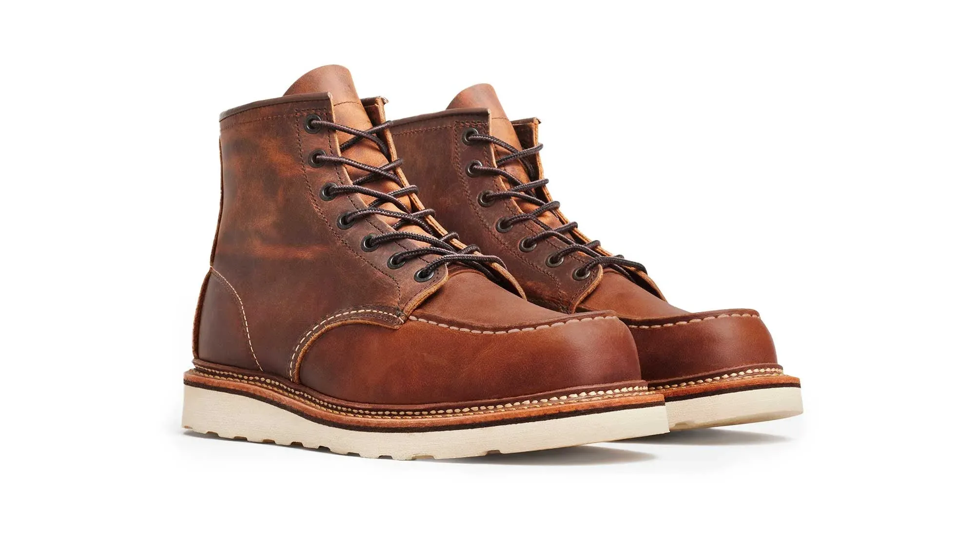A pair of copper leather moc toe boots on cream wedge soles, seen from the front at an angle