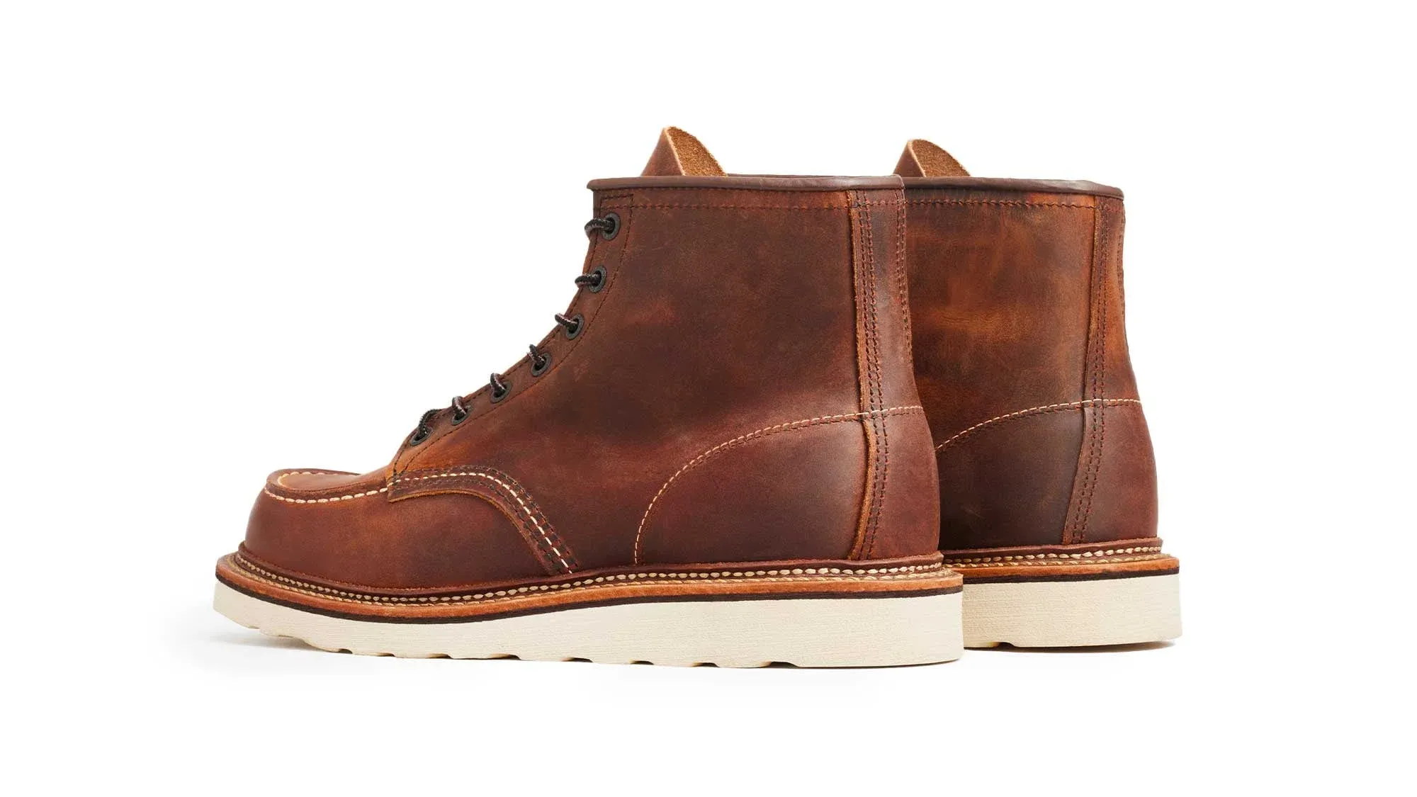A pair of copper leather moc toe boots on cream wedge soles, seen from behind at an angle