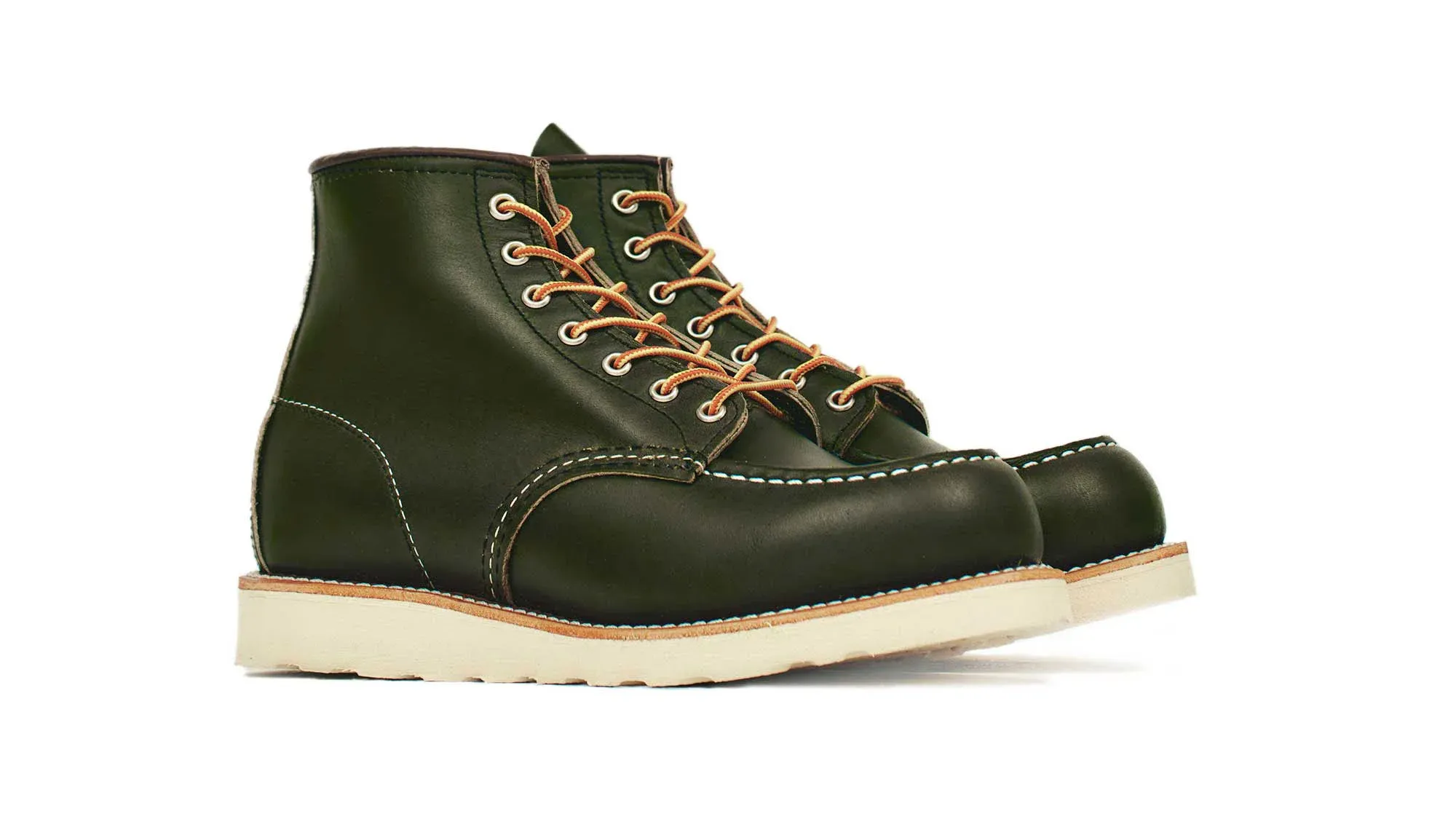 A pair of forest green leather moc toe boots on cream wedge soles, seen from the front at an angle