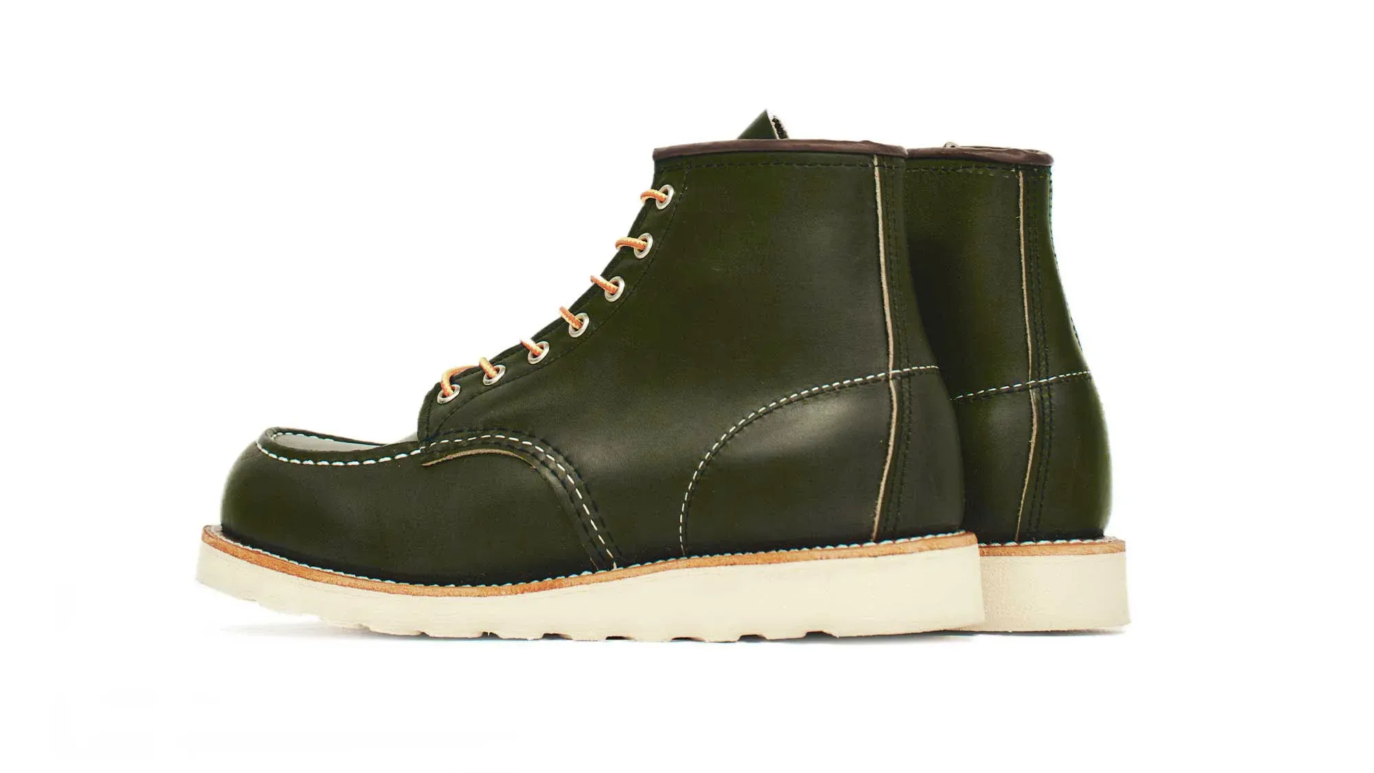 A pair of forest green leather moc toe boots on cream wedge soles, seen from behind at an angle